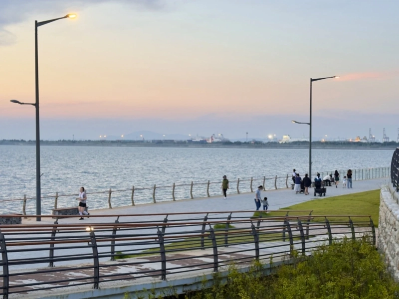 夕暮れの空の下、海沿いの遊歩道を散策する人々と、水平線までひらけた海
